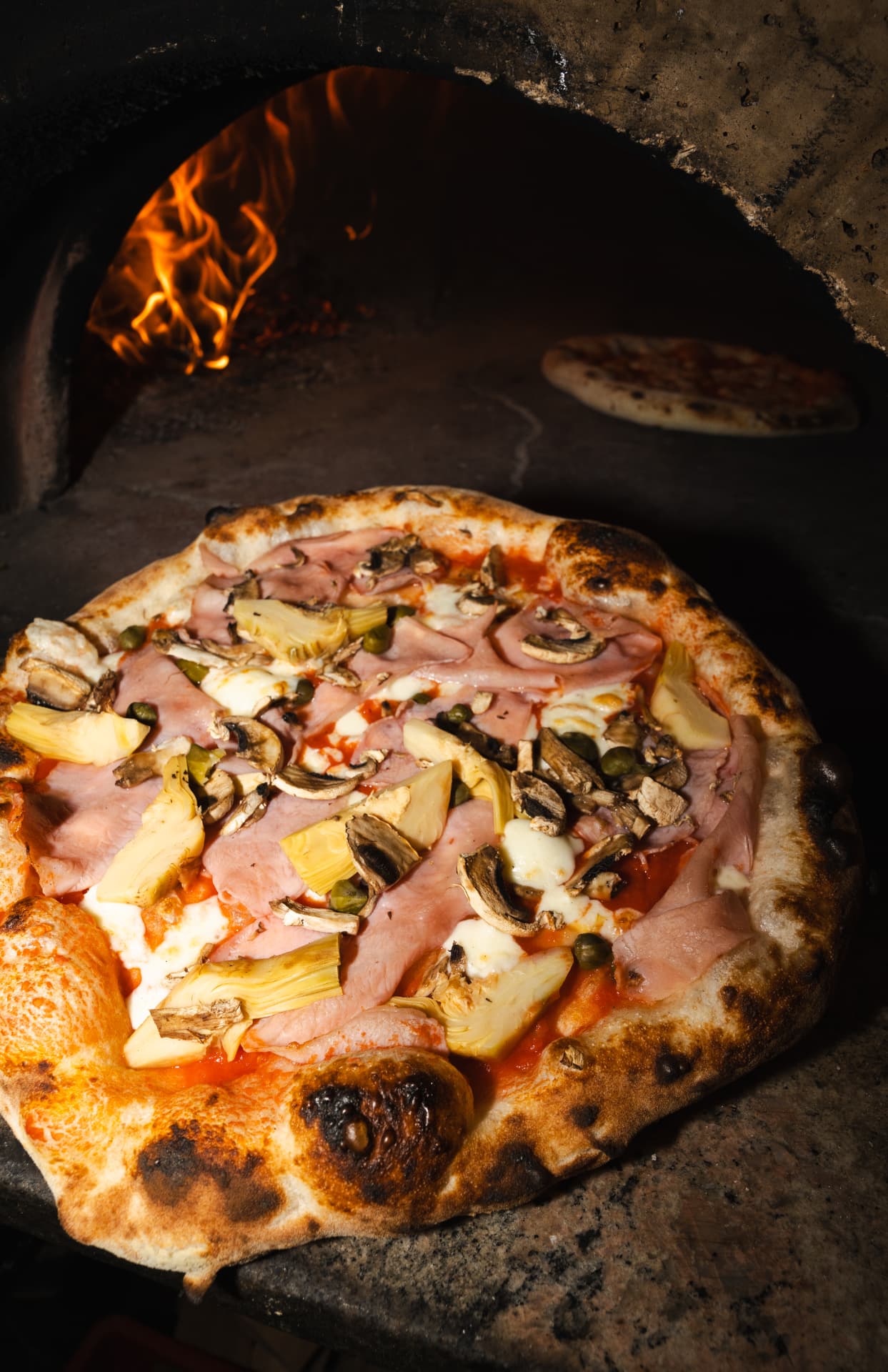 Belegte Pizza aus dem Holzofen auf dem Ofenstein
