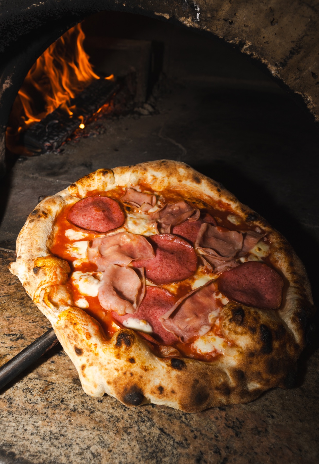 Pizza aus dem Holzofen, im Hintergrund lodert das Feuer